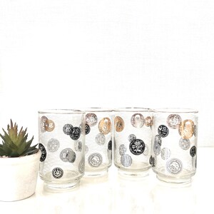 May include: Set of four clear glass tumblers with a silver and gold coin design. The glasses have a textured surface and a rounded base.