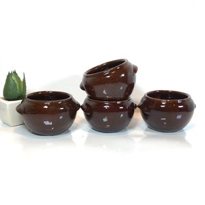 May include: Four brown ceramic bowls with small handles on the sides. The bowls are arranged in a row, with two stacked on top of each other.
