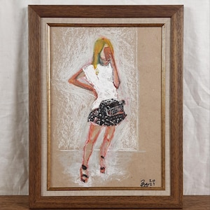 May include: A framed pastel artwork. The drawing shows a figure wearing a white top and black patterned shorts. The artwork is set against a neutral background and is signed in the bottom right corner.