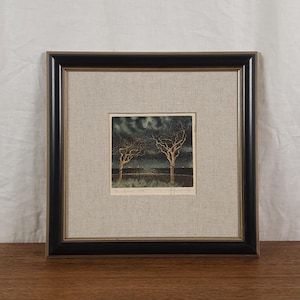 May include: A framed print featuring a dark, nocturnal landscape with two bare trees under a crescent moon. The artwork is set within a light-colored linen mat and a black frame with a thin gold inner border, creating a square composition.