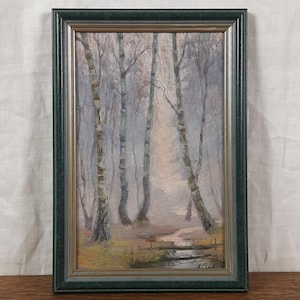 May include: An oil painting of a misty forest scene, framed in a dark green wooden frame with a gold inner edge. The artwork depicts tall, slender birch trees with a stream winding through the forest floor. The color palette is muted, with soft blues, greens, and browns.
