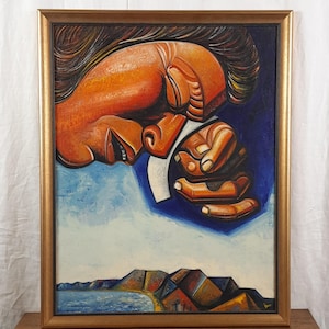 May include: An oil painting in a gold frame depicting a large, stylized orange face in profile with eyes closed, resting a hand against the cheek. Below, a blue sea meets a shoreline with dark, angular mountains under a light blue sky.