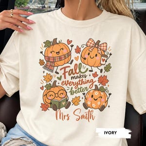 May include: An ivory t-shirt featuring a graphic of four cartoon pumpkins with autumn leaves and the text "Fall makes everything better" and "Mrs Smith". One pumpkin wears a scarf, one has a bow and coffee, one wears glasses reading a book, and one has flowers.