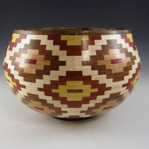 May include: A handcrafted wooden bowl with a geometric pattern. The bowl features a mosaic design with alternating colors of red, yellow, brown, and natural wood tones. The bowl's diameter is approximately 10 inches.