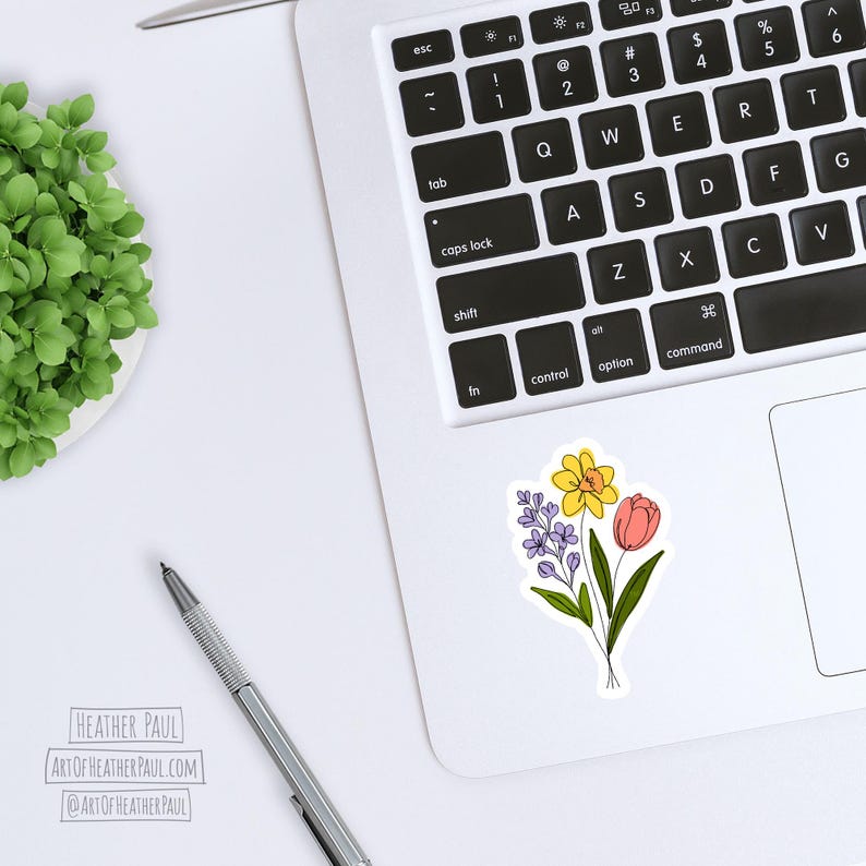 sticker featuring a purple freesia, a yellow daffodil with and orange center and a  pinkish-red tulip mocked up on a laptop computer