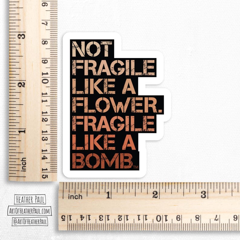 sticker reading "not fragile like a flower. fragile like a bomb" in a warm gradient over a white background with brown rulers to show sizing