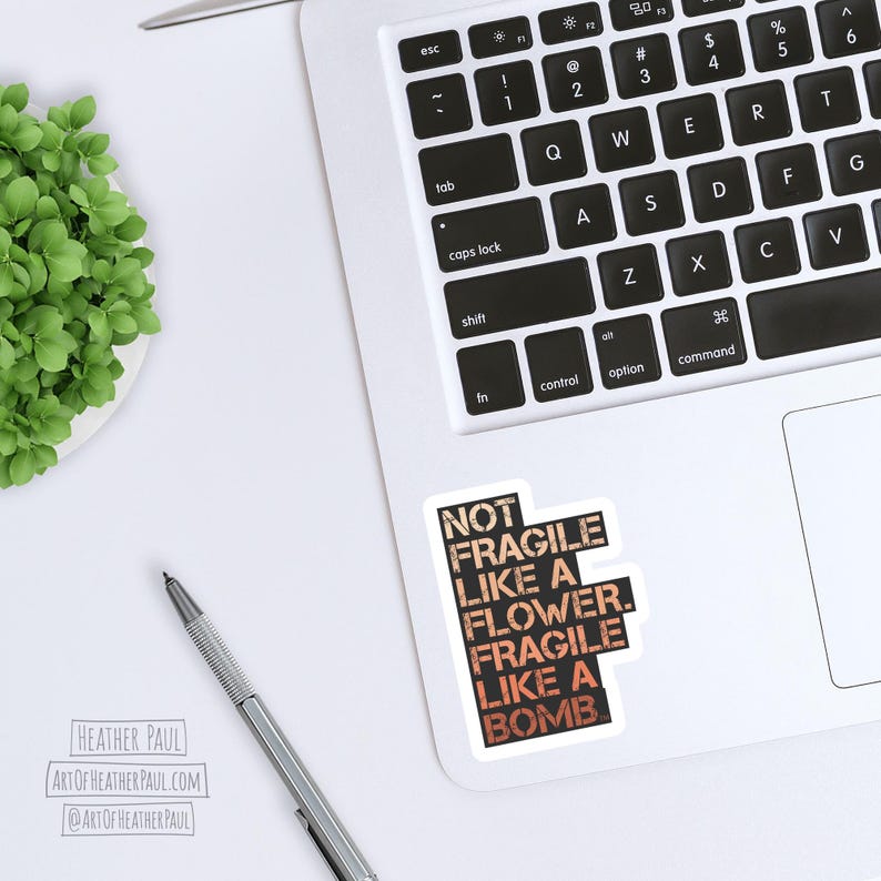 sticker reading "not fragile like a flower. fragile like a bomb" in a warm gradient mocked up on a laptop computer