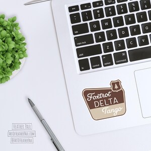 sticker featuring a national parks style sign with the text reading the phrase foxtrot delta tango mocked up on a laptop computer