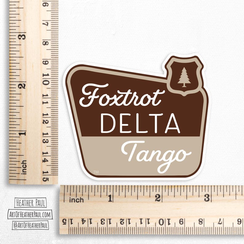sticker featuring a national parks style sign with the text reading the phrase foxtrot delta tango over a white background with brown rulers to show sizing
