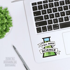 Pode incluir: Um computador port&aacute;til branco com um adesivo verde e azul com tema cient&iacute;fico no touchpad. O adesivo apresenta um b&eacute;quer com o texto "Y'all Need Science".