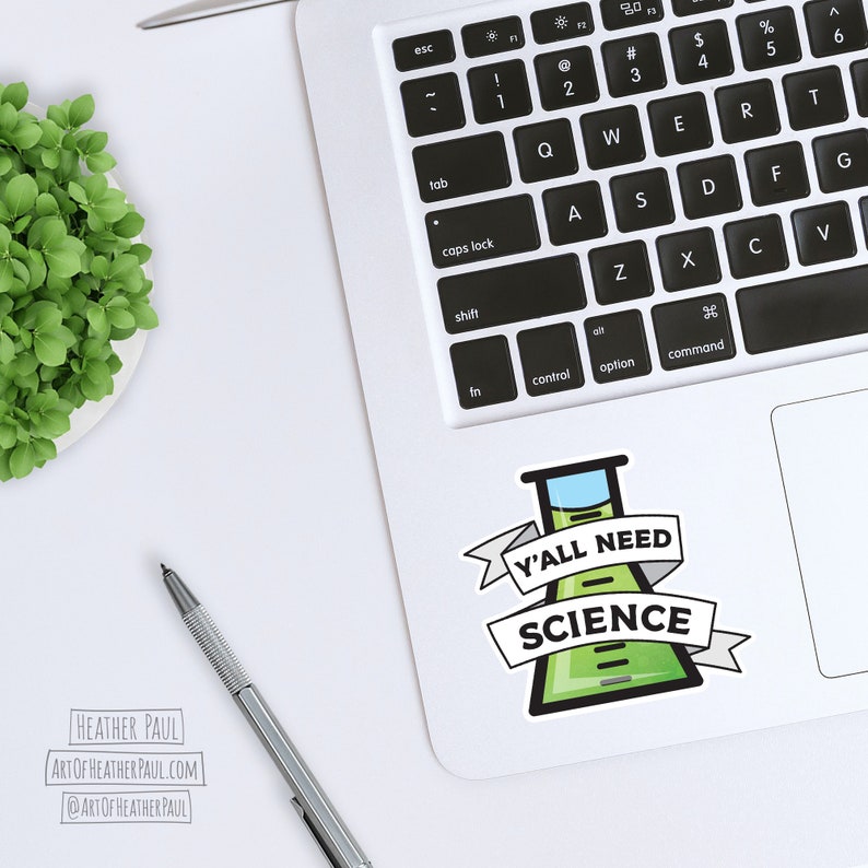Pode incluir: Um computador port&aacute;til branco com um adesivo verde e azul com tema cient&iacute;fico no touchpad. O adesivo apresenta um b&eacute;quer com o texto "Y'all Need Science".