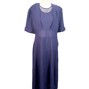 May include: A navy blue dress with a sheer midsection and a beaded neckline. The dress has short sleeves and a flowing skirt. The dress is displayed on a mannequin.