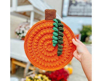Puede incluir: Una calabaza naranja de ganchillo con un tallo verde. La calabaza está hecha con un punto texturizado y tiene una forma redonda.