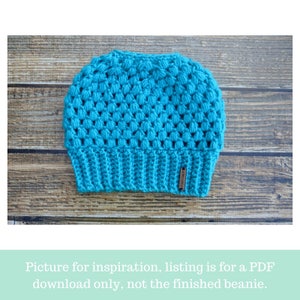 crochet messy bun beanie laying flat on wooden backdrop in the color turquoise