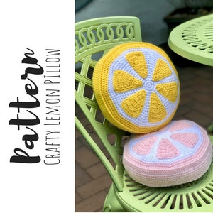 May include: Two crocheted lemon-shaped pillows, one yellow and one pink, are sitting on a green chair. The yellow pillow has a white center and the pink pillow has a white center. The chair is made of metal and has a woven pattern.