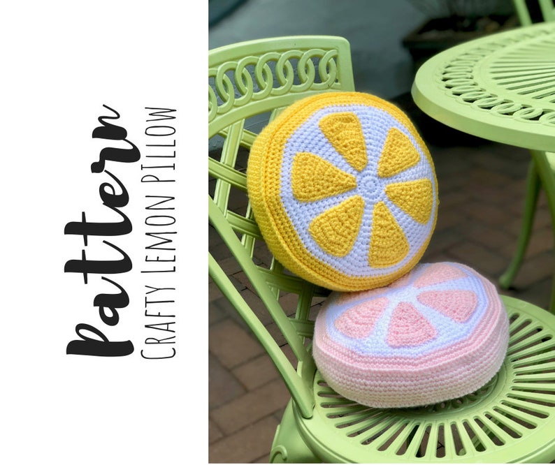 May include: Two crocheted lemon-shaped pillows, one yellow and one pink, are sitting on a green chair. The yellow pillow has a white center and the pink pillow has a white center. The chair is made of metal and has a woven pattern.