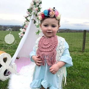 Caucasian baby girl wearing a rosy pink crochet baby bib, a blue shirt and a flower crown.  Listing is for a crochet bib pattern and not the finished baby bib.