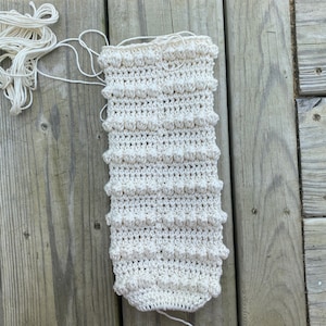 May include: A close-up of a crocheted white fabric with a textured pattern. The fabric is lying on a wooden surface.