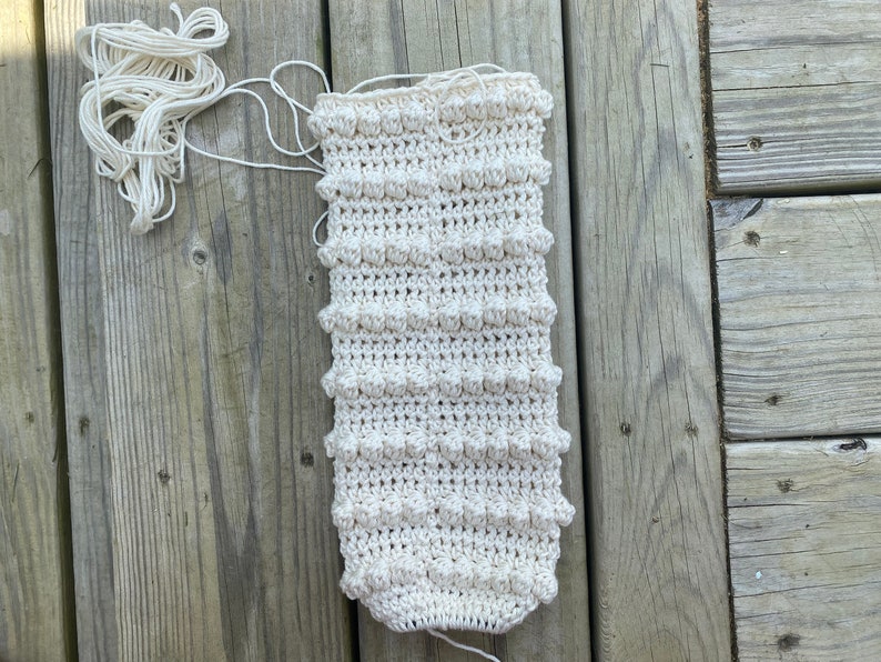 May include: A close-up of a crocheted white fabric with a textured pattern. The fabric is lying on a wooden surface.