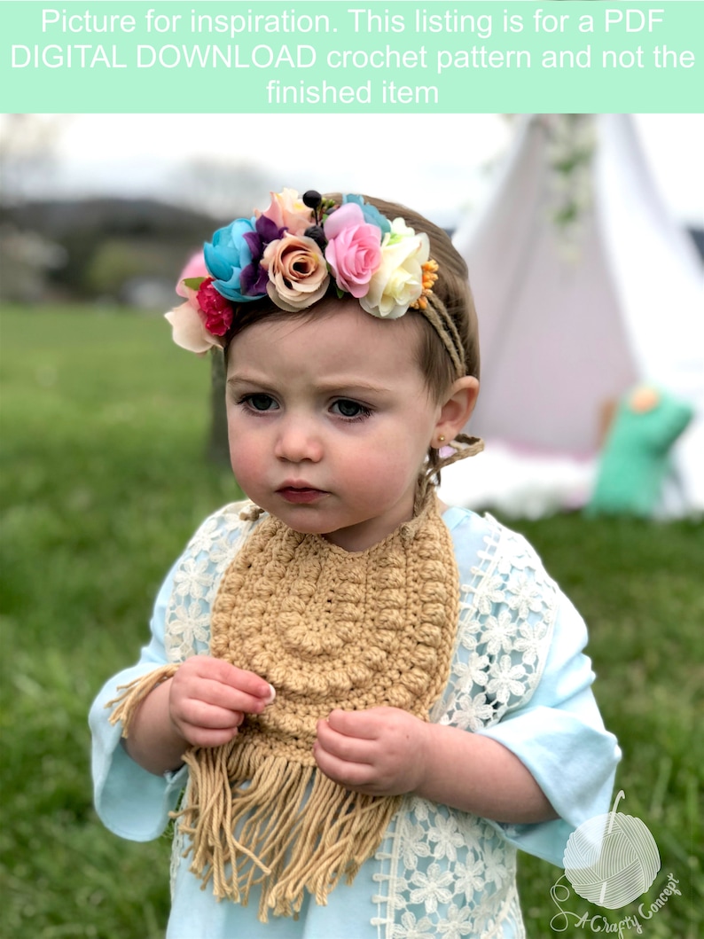 Caucasian baby girl wearing a dark tan crochet baby bib, a blue shirt and a flower crown.  Listing is for a crochet bib pattern and not the finished baby bib.