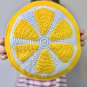 May include: A crocheted lemon-shaped pillow with yellow and white yarn. The pillow is round and has a 3D design.