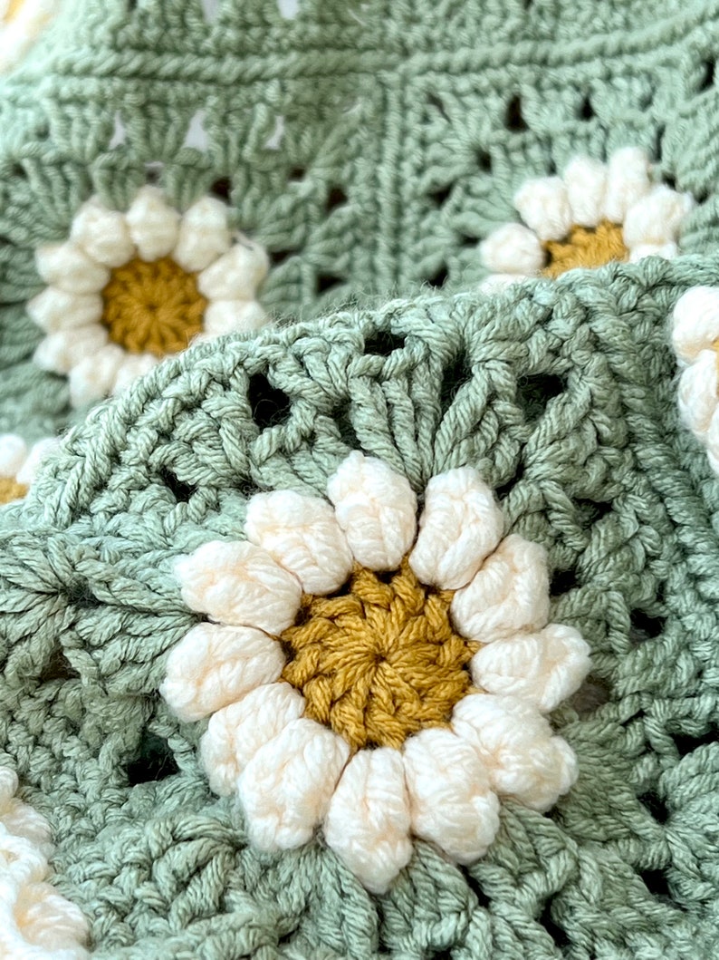 Daisy granny square blanket with a green background, white petals, and a yellow center. The listing is for a digital download crochet pattern and not the finished blanket.