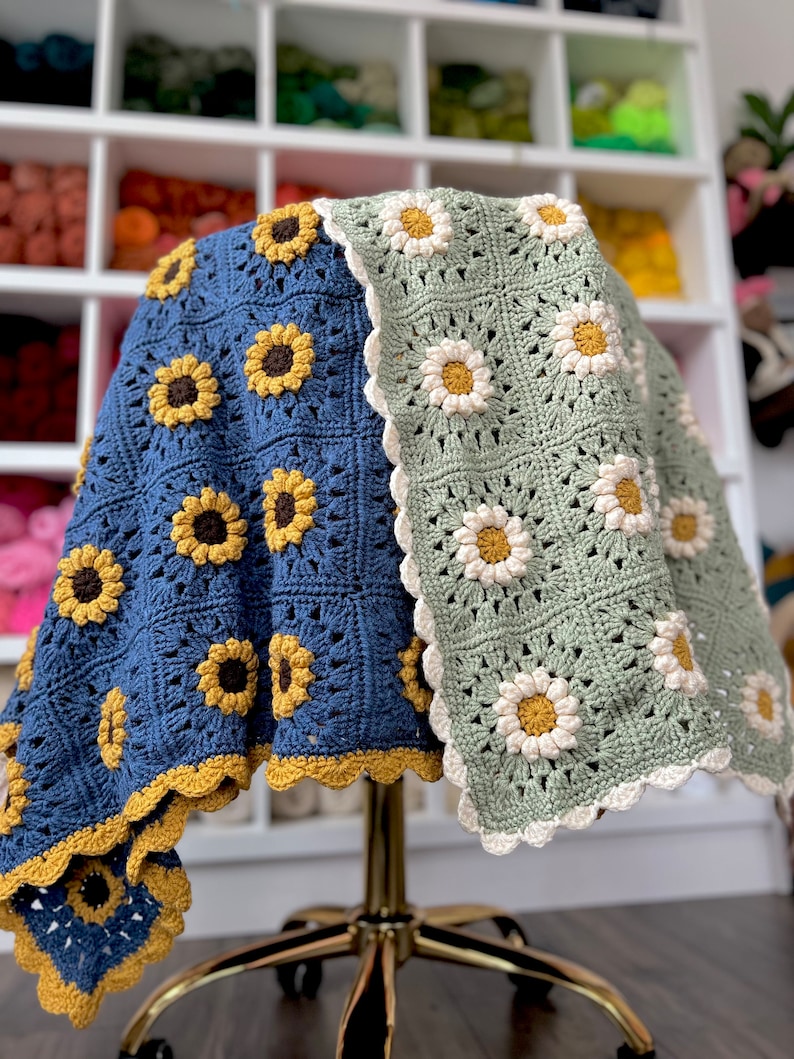 May include: A crocheted blanket with a blue and green background featuring a sunflower and daisy pattern. The blanket has a scalloped edge.