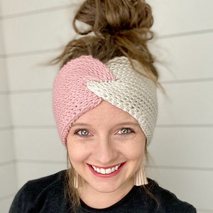 Può includere: Un cerchietto di maglia rosa e bianco con un design intrecciato. Il cerchietto è indossato da una persona con i capelli castani.