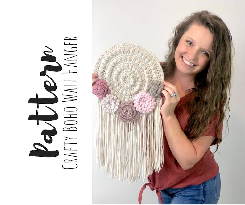 Puede incluir: Un tapiz de pared de ganchillo con un dise&ntilde;o circular y flores rosas. El tapiz tiene una franja de hilo blanco. El texto "Crafty Boho Wall Hanger" y "Pattern" es visible en la imagen.