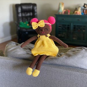 Crochet doll with dark skin wearing a yellow dress, yellow shoes and bright pink hair. Listing is for a crochet doll pattern and not the finished piece.