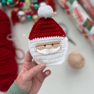 May include: A crocheted Santa Claus ornament with a white pom-pom hat, red hat, white beard, and black eyes.