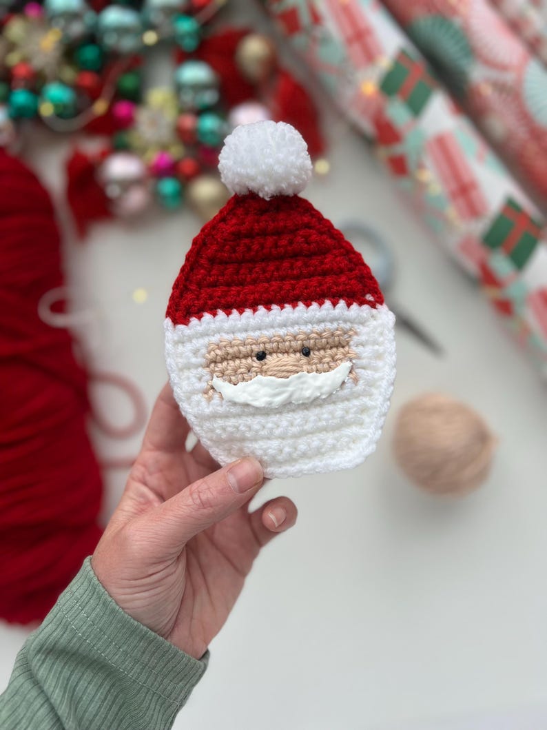 May include: A crocheted Santa Claus ornament with a white pom-pom hat, red hat, white beard, and black eyes.