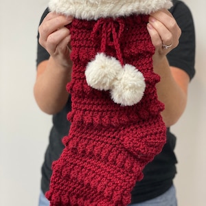 May include: A red crocheted Christmas stocking with white faux fur trim and white pom-poms.