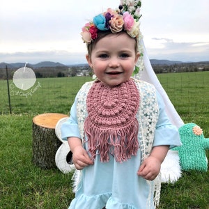 Caucasian baby girl wearing a rosy pink crochet baby bib, a blue shirt and a flower crown.  Listing is for a crochet bib pattern and not the finished baby bib.