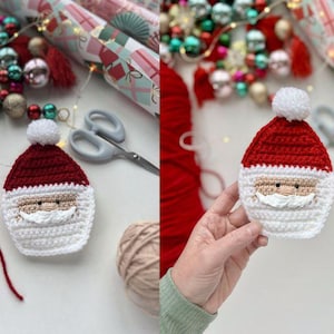 May include: A crocheted Santa Claus ornament with a red hat, white beard, and black eyes. The ornament is held in a hand against a white background.