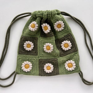 Puede incluir: Una bolsa de cord&oacute;n de crochet verde con un patr&oacute;n de margarita. La bolsa tiene un cord&oacute;n largo de color verde.