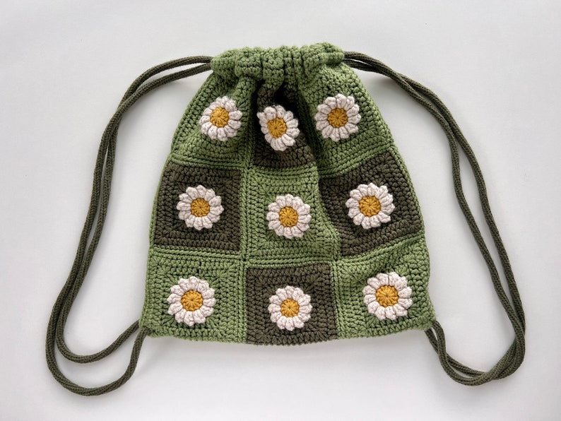 Puede incluir: Una bolsa de cord&oacute;n de crochet verde con un patr&oacute;n de margarita. La bolsa tiene un cord&oacute;n largo de color verde.