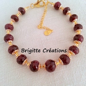 May include: A gold bracelet with a chain clasp and red gemstone beads. The beads are faceted and have a gold trim. The bracelet is labeled "Brigitte Créations".
