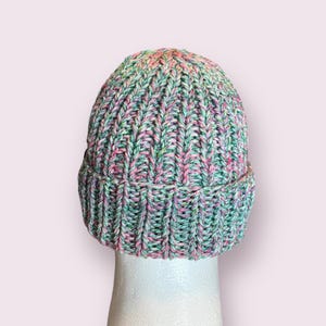 May include: A green, pink, and white knit beanie hat with a ribbed texture. The hat is on a white mannequin head.