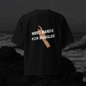 May include: Black t-shirt with white text that reads "Need Bands For Bangles" and a graphic of a hand with bangles.