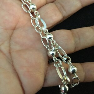 May include: A silver chain necklace with oval and round links. The chain has a silver bead at each link.