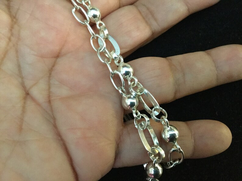 May include: A silver chain necklace with oval and round links. The chain has a silver bead at each link.