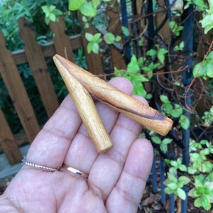 May include: A wooden carving in the shape of a V, with a natural wood finish and dark brown streaks. The carving is held in a hand.