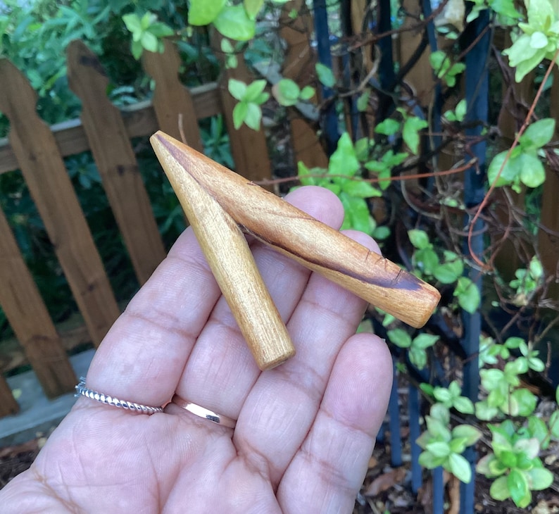 May include: A wooden carving in the shape of a V, with a natural wood finish and dark brown streaks. The carving is held in a hand.