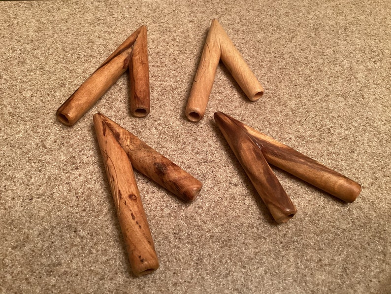 May include: Four wooden arrowheads with a v-shaped design. The arrowheads are made of light and dark brown wood.