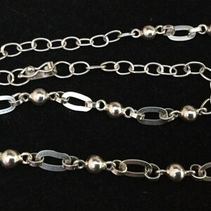 May include: A silver chain necklace with oval links and round beads.