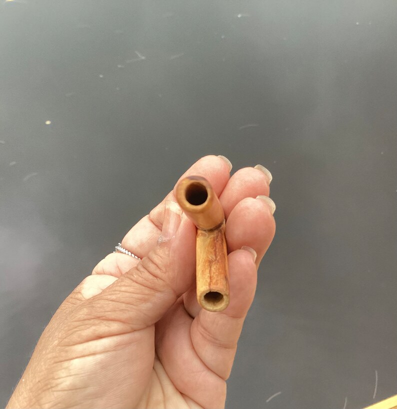 May include: A wooden pipe with a brown and natural finish. The pipe has a curved stem and a round bowl.