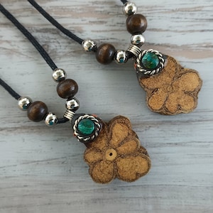 Può includere: Due collane con perline di legno e ciondoli a forma di fiore. Ogni ciondolo ha una pietra preziosa verde al centro.