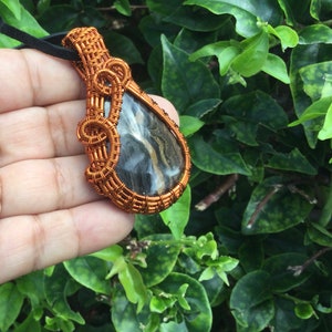 May include: A teardrop-shaped pendant with a black and brown stone wrapped in copper wire.