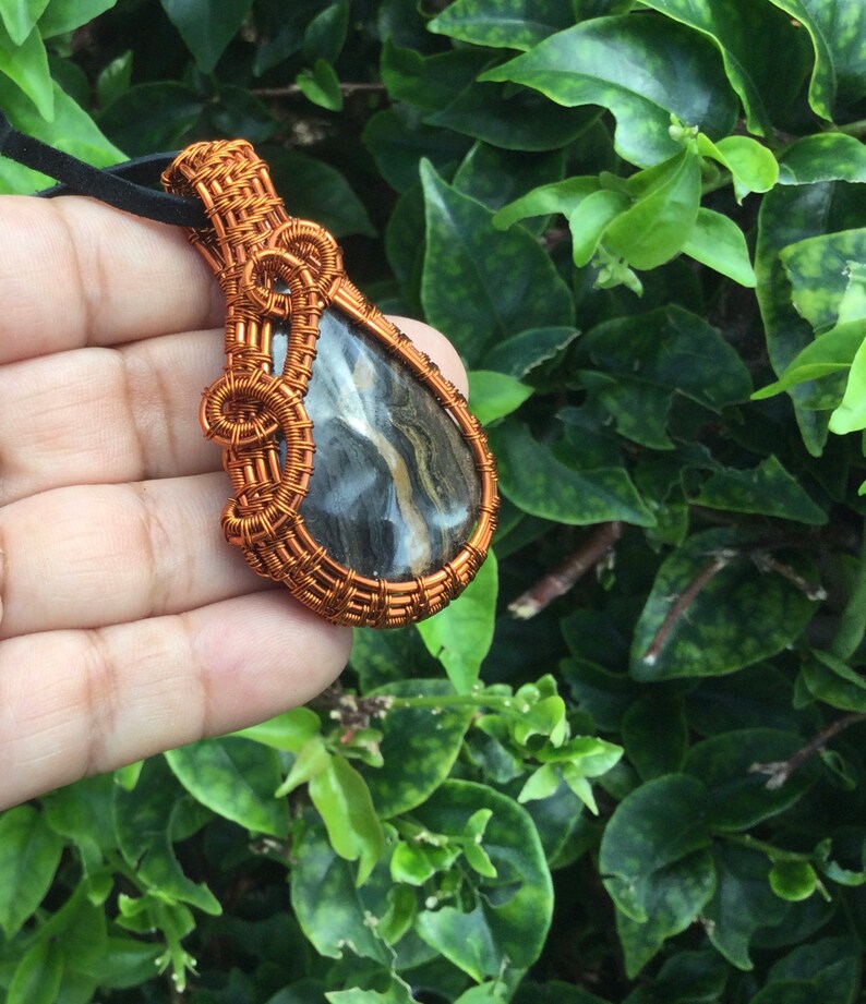 May include: A teardrop-shaped pendant with a black and brown stone wrapped in copper wire.